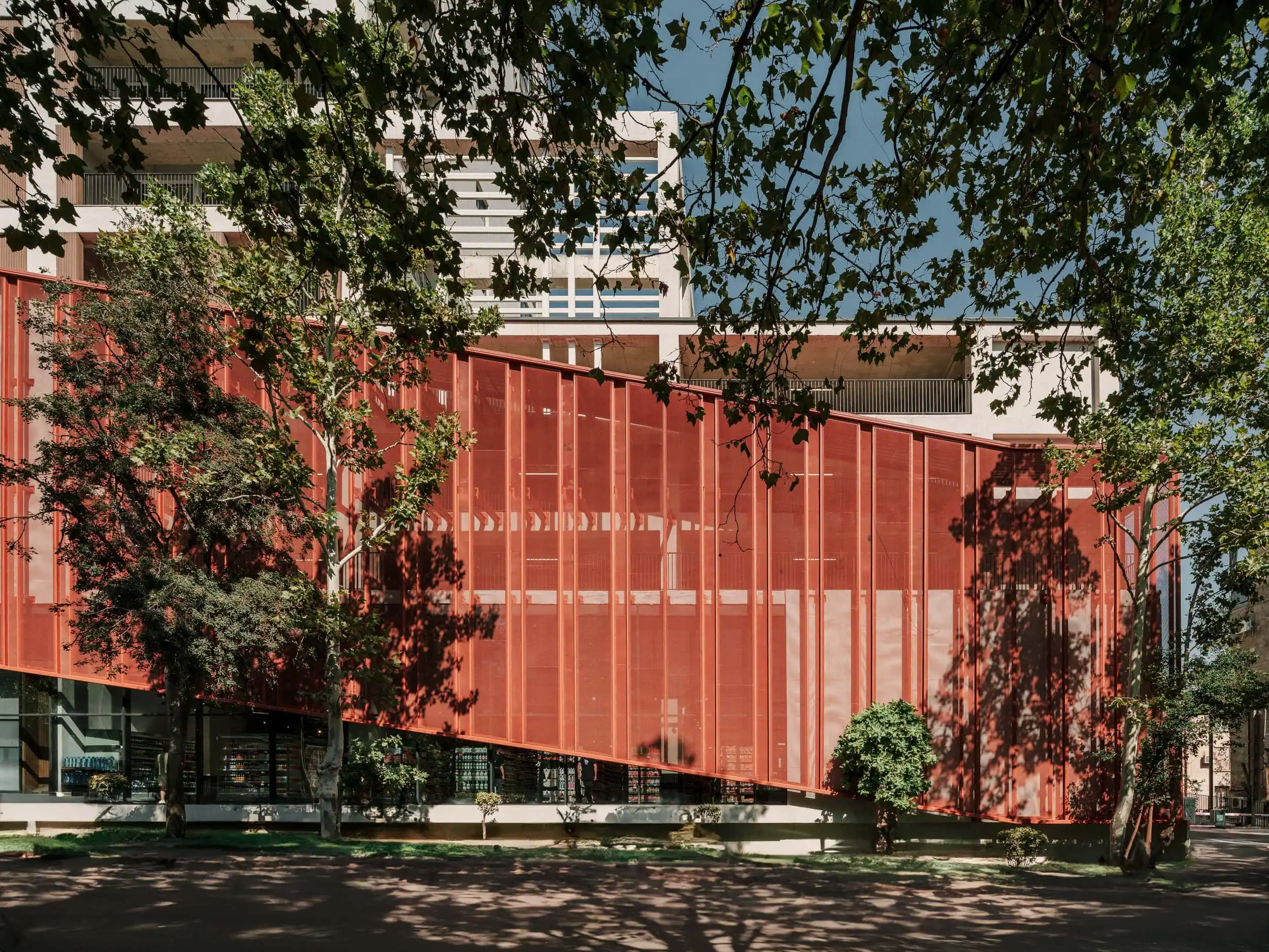 Modern architectural building with red facade and surrounding greenery, located in urban setting.