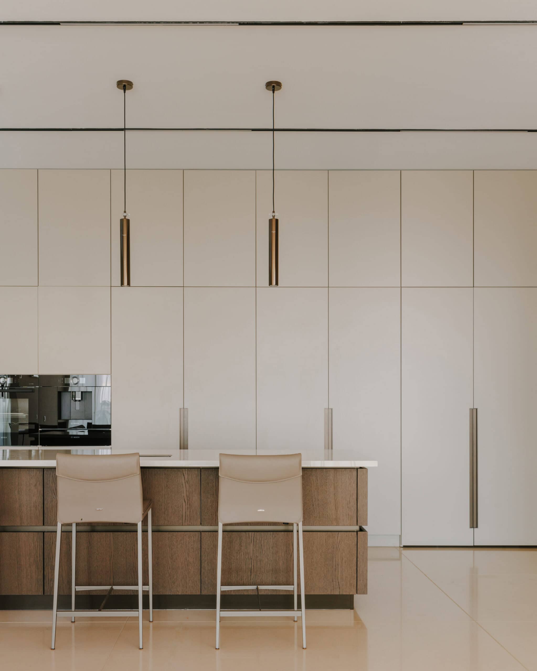 Minimalist modern kitchen interior with beige and wooden accents, pendant lighting, and sleek cabinetry.