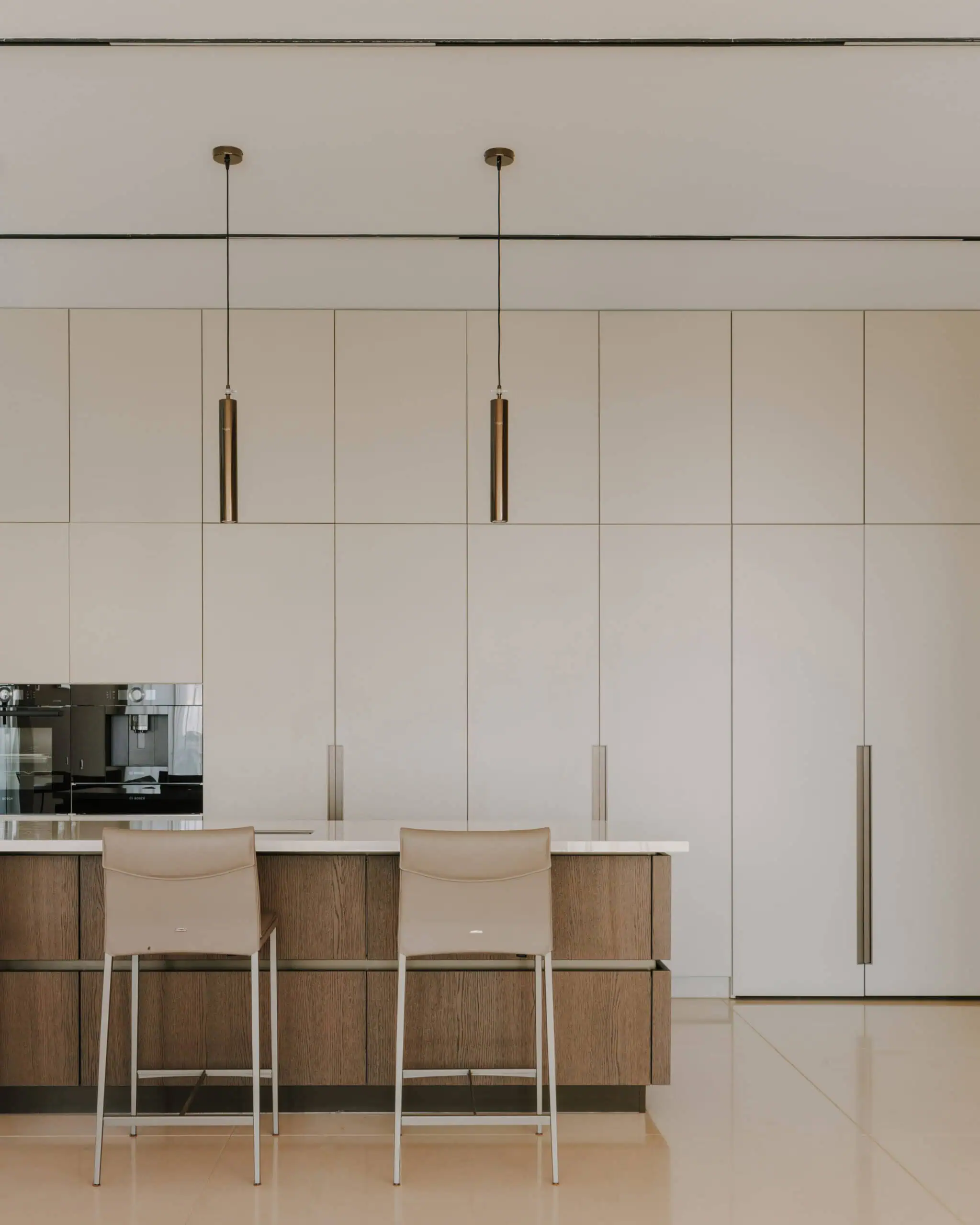 Minimalist modern kitchen interior with beige and wooden accents, pendant lighting, and sleek cabinetry.