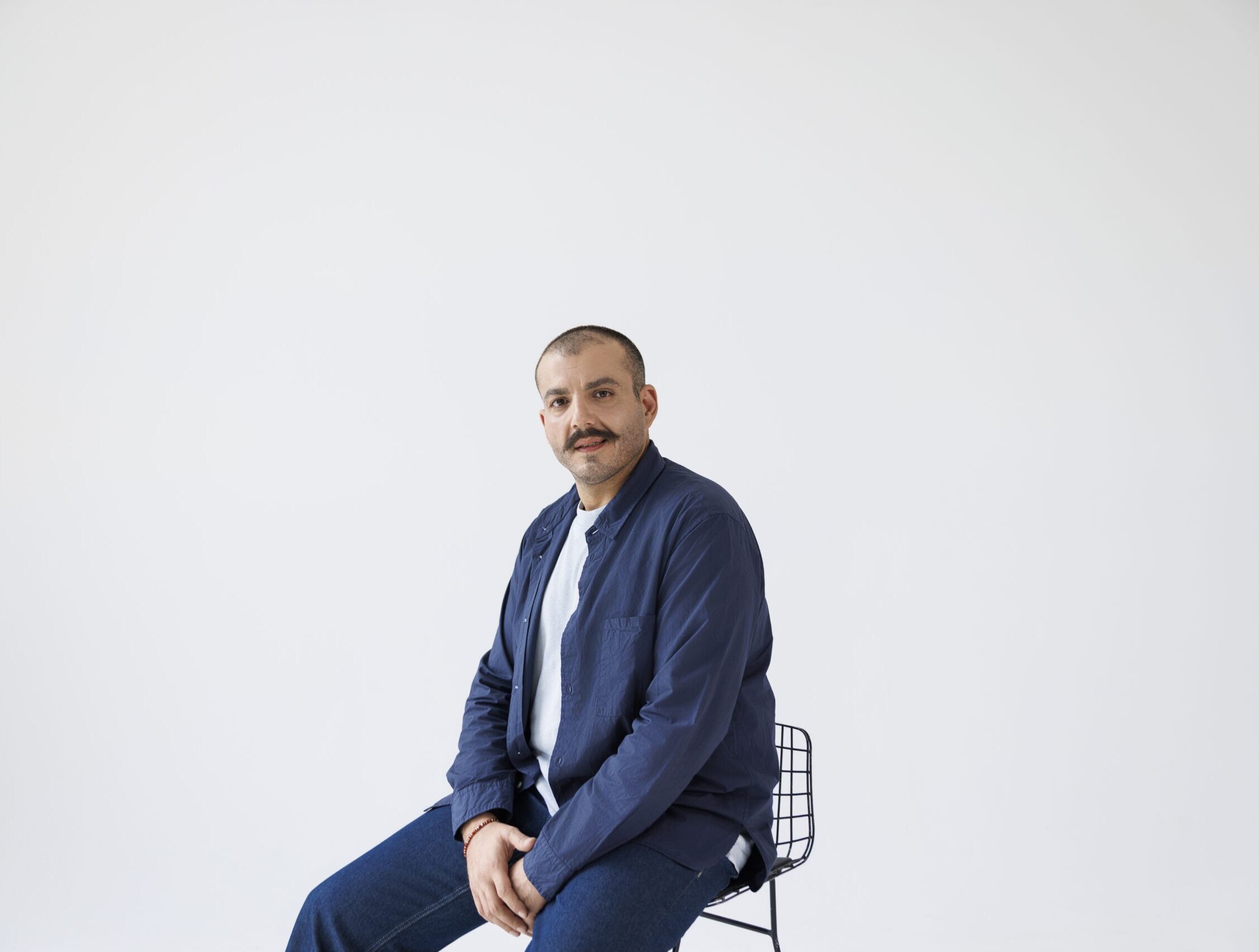 Man sitting on a stool in a studio with a plain white background.