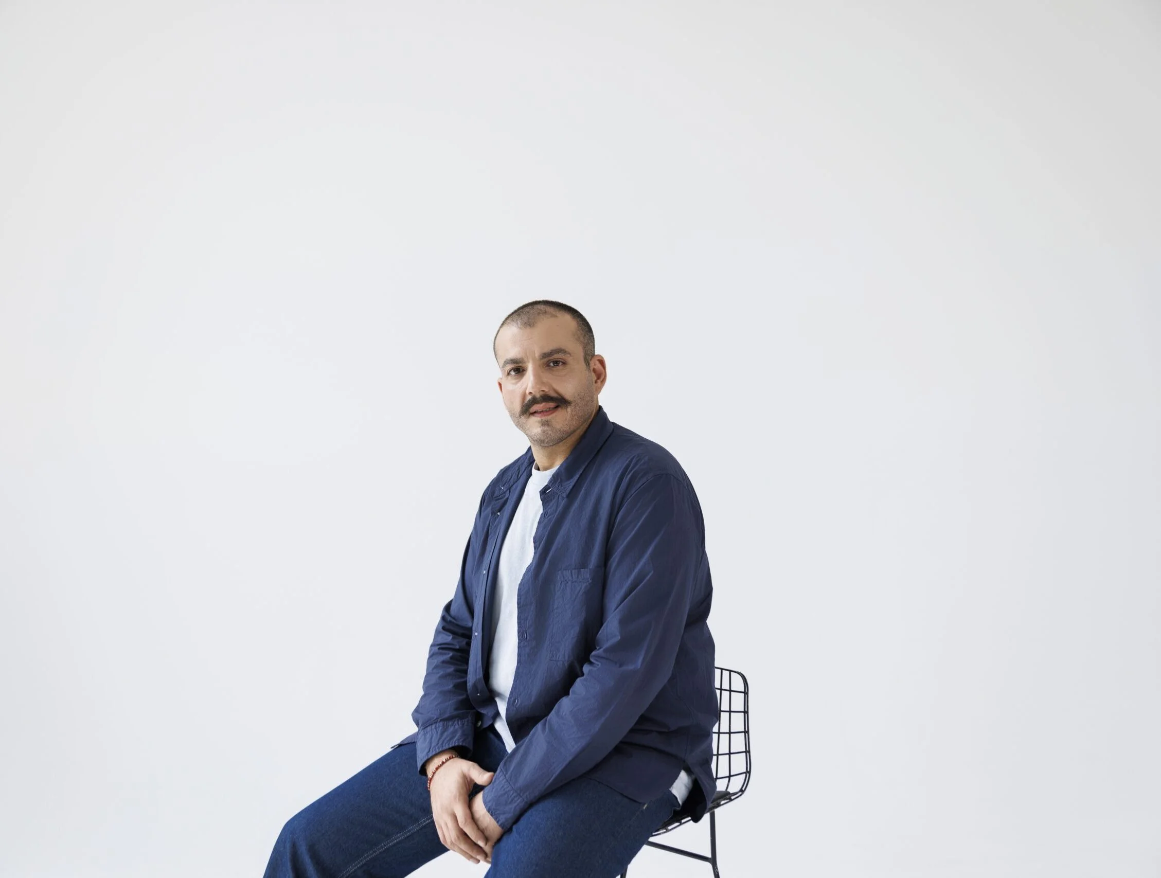 Man sitting on a stool in a studio with a plain white background.