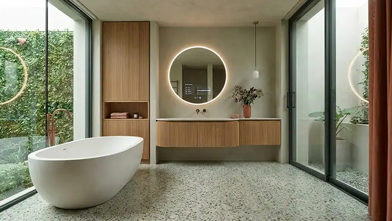 Elegant modern bathroom with freestanding bathtub, circular mirror, and floor-to-ceiling glass windows.