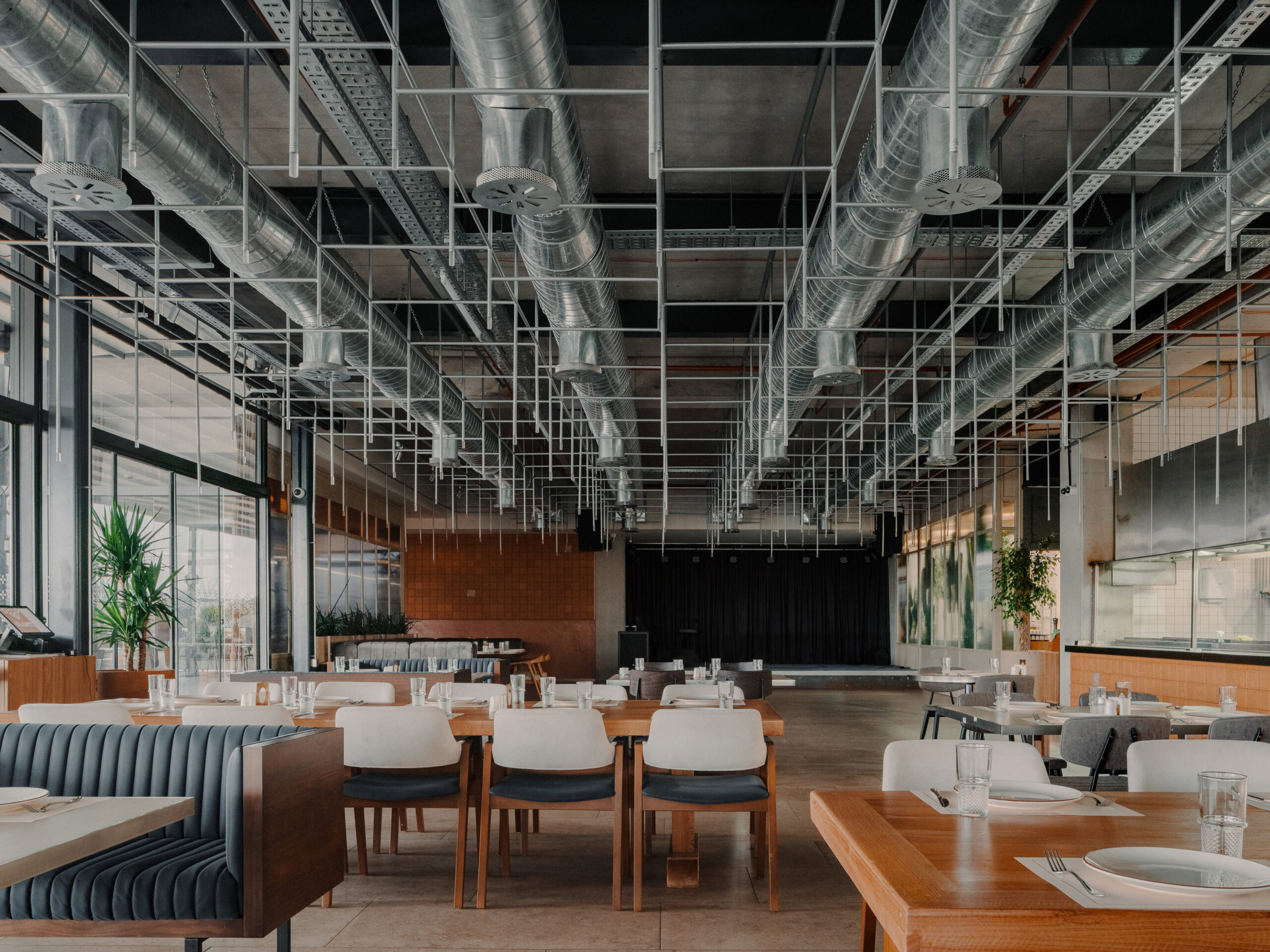 Spacious modern restaurant interior with industrial ceiling design and natural lighting.